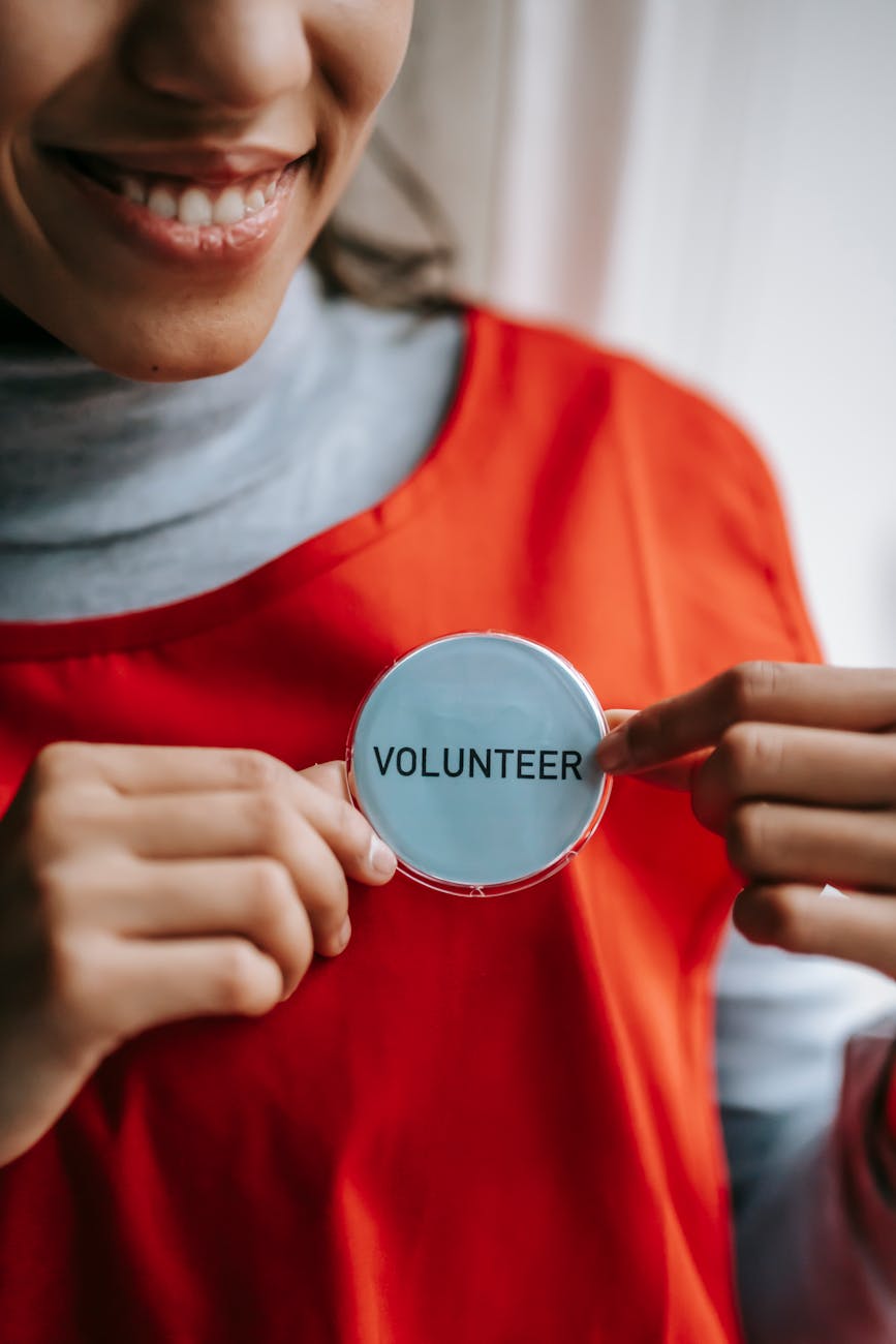 smiling ethnic woman showing volunteer sign on red apron